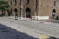 an intersection with a brick road and building in background and another street sign near by