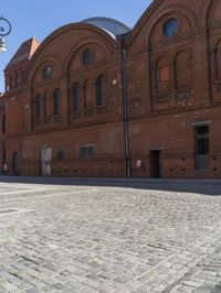 a brick road leading to an old building with tall windows and a clock on each side