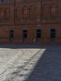 a brick road leading to an old building with tall windows and a clock on each side