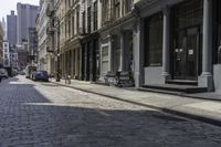 a brick road in an old - fashioned town with cars parked and people walking by it