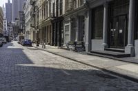 a brick road in an old - fashioned town with cars parked and people walking by it