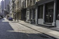 a brick road in an old - fashioned town with cars parked and people walking by it