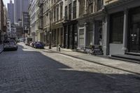 a brick road in an old - fashioned town with cars parked and people walking by it