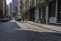 a brick road in an old - fashioned town with cars parked and people walking by it