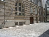 a brick sidewalk in front of a large building with windows on it and the ground is cobblestone