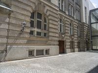 a brick sidewalk in front of a large building with windows on it and the ground is cobblestone