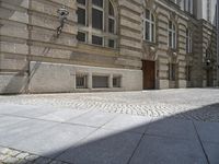 a brick sidewalk in front of a large building with windows on it and the ground is cobblestone