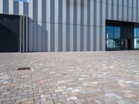 the sidewalk is made out of bricks with a clock in front of the building on the right side