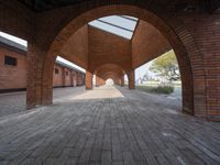 an empty brick walkway in between two arches with a skylight above and a path leading to the building