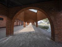 an empty brick walkway in between two arches with a skylight above and a path leading to the building