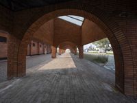 an empty brick walkway in between two arches with a skylight above and a path leading to the building