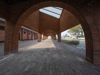 an empty brick walkway in between two arches with a skylight above and a path leading to the building