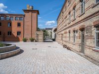 a brick walkway in an old brick building courtyard with a bench and firepith