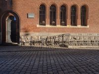 brick walkway leading to a red brick building with black doors and a white bike parked next to it
