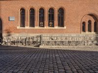 brick walkway leading to a red brick building with black doors and a white bike parked next to it