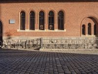 brick walkway leading to a red brick building with black doors and a white bike parked next to it