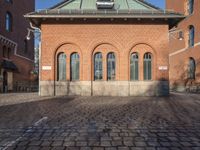 brick walkway leading to a red brick building with black doors and a white bike parked next to it