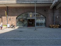 a brick walkway that goes into a building with people on benches in front of it