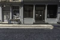 a brick walkway in front of a building with graffiti on it in the sunlight and a yellow umbrella by it