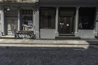 a brick walkway in front of a building with graffiti on it in the sunlight and a yellow umbrella by it