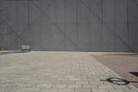 a brick walkway in front of an unfinished building with a bench outside it and in the foreground is a square pattern with squares of gray tiles on it