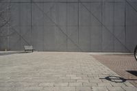 a brick walkway in front of an unfinished building with a bench outside it and in the foreground is a square pattern with squares of gray tiles on it