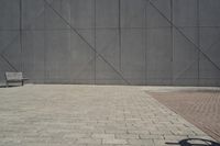 a brick walkway in front of an unfinished building with a bench outside it and in the foreground is a square pattern with squares of gray tiles on it