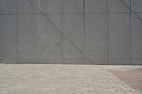 a brick walkway in front of an unfinished building with a bench outside it and in the foreground is a square pattern with squares of gray tiles on it