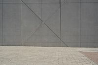 a brick walkway in front of an unfinished building with a bench outside it and in the foreground is a square pattern with squares of gray tiles on it