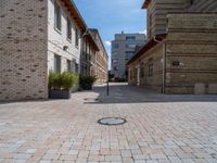 an empty street has bricks on the ground near buildings and a circle in the middle of the sidewalk