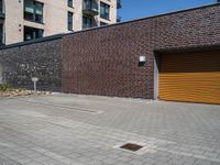 two men with orange safety helmets riding skateboards in front of a building, a yellow garage door and a brick sidewalk