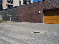 two men with orange safety helmets riding skateboards in front of a building, a yellow garage door and a brick sidewalk