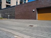 two men with orange safety helmets riding skateboards in front of a building, a yellow garage door and a brick sidewalk