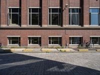 an empty brick driveway has three motorcycles parked by the front of it and bicycles in the background