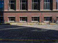 an empty brick driveway has three motorcycles parked by the front of it and bicycles in the background