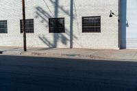 the shadow of a tree on the side of a building by a road with a car parked on it