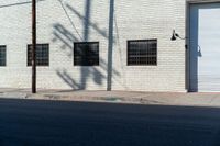 the shadow of a tree on the side of a building by a road with a car parked on it