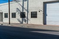 the shadow of a tree on the side of a building by a road with a car parked on it