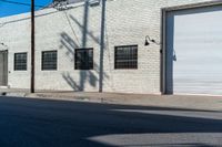 the shadow of a tree on the side of a building by a road with a car parked on it