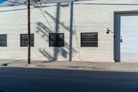 the shadow of a tree on the side of a building by a road with a car parked on it