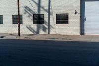 the shadow of a tree on the side of a building by a road with a car parked on it