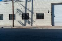 the shadow of a tree on the side of a building by a road with a car parked on it