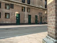 a couple of men walking past a brick building with several green doors on the other side