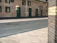 a couple of men walking past a brick building with several green doors on the other side