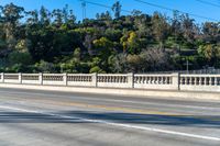 a long bridge near trees and mountains with a bench on one side and a small road on the other