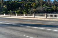 a long bridge near trees and mountains with a bench on one side and a small road on the other