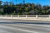 a long bridge near trees and mountains with a bench on one side and a small road on the other