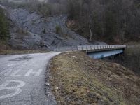 a bridge spanning the mountains to pass over a dirt road with a rock hill on either side