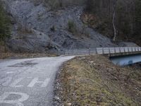 a bridge spanning the mountains to pass over a dirt road with a rock hill on either side