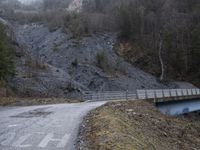 a bridge spanning the mountains to pass over a dirt road with a rock hill on either side